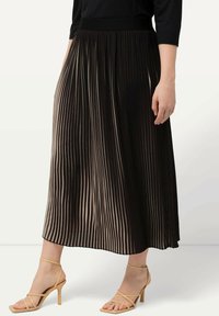 Gonna maxi plissè nera e taupe, realizzata in un tessuto testurizzato con elastico in vita. Indossata con sandali alti beige con lacci.