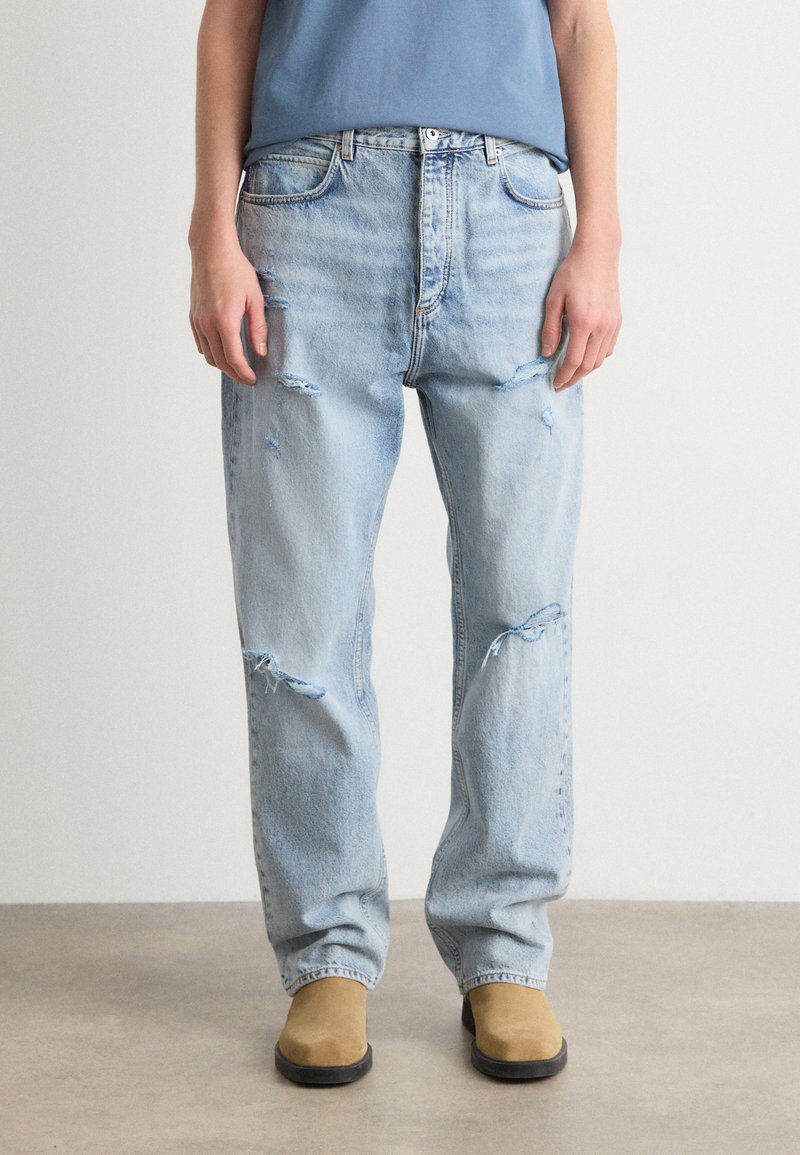 Jeans de denim azul claro, desgastados, con un corte relajado y detalles rasgados. Combinados con botas de ante color beige hasta el tobillo.