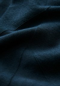 Mørkeblåt stof med et struktureret strikmønster, der fremhæver glatte og let hævede overflader, hvilket understreger dybde og dimension.