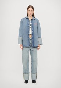 Denim krekls un džinsi komplekts, gaismas zilā krāsā, ar brīvu piegriezumu, pogu aizdari, platām piedurknēm un kontrastējošiem diegiem apakšmalā. Melni apavi.