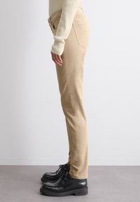 Beige suorat lahkeet, joissa on pehmeä rakenne ja keskikorkea vyötärö, yhdistetty mustiin nauhakenkiin, joissa on paksu pohja.