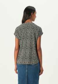 Short-sleeve top in black and white patterned fabric, featuring a relaxed fit and rounded hem, paired with a denim skirt.