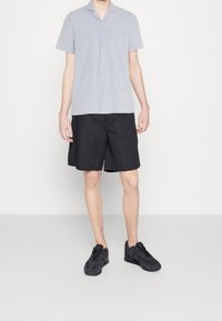 Jasnoniebieska i biała, w paski, koszula z krótkim rękawem z kołnierzykiem, w połączeniu z czarnymi szortami do kolan i czarnymi butami sportowymi.