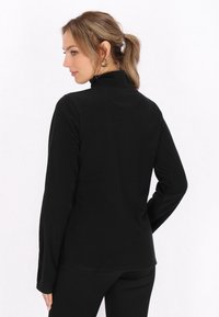 Zwarte lange mouw top met hoge kraag, gemaakt van zacht materiaal, met een gladde textuur en slim fit, weergegeven vanuit de achterkant.