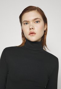 Svart ribbestrikket turtleneck genser med en tettsittende design. Lange ermer og en høy krage skaper en strømlinjeformet silhuett og tekstur.