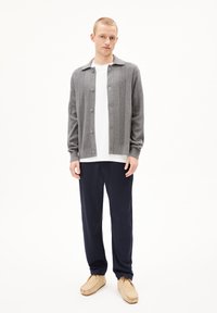 Gilet gris à boutons avec une texture côtelée subtile, porté sur un t-shirt blanc et associé à un pantalon bleu marine et des chaussures slip-on beiges.