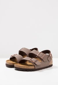 Sandalias marrones con dos correas anchas y hebillas ajustables, que presentan una plantilla de corcho y una suela de goma texturizada. Acabado suave y diseño sencillo.