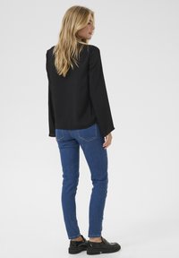 Sort langærmet top med afslappet pasform, parret med blå skinny jeans og sorte platform sko, set bagfra.