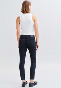 Schwarze Skinny-Jeans aus Denim mit mittlerer Taille und Gesäßtaschen. Kombiniert mit einem weißen Tanktop und schwarzen Slippers.