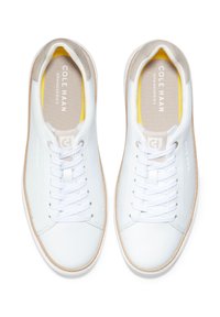 Sneaker in pelle bianca con punta rotonda, chiusura con lacci, accenti beige e suole in gomma testurizzata. L'interno è dotato di una morbida fodera gialla.