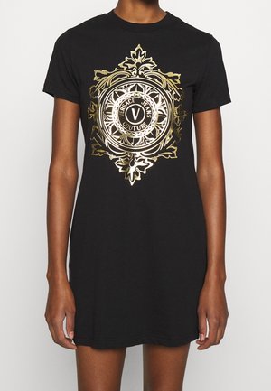 Robe t-shirt noire avec un logo ornemental doré au centre, manches courtes et coupe décontractée, confectionnée en coton doux.