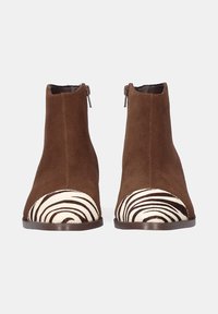 Botas de tobillo de ante marrón con una puntera de pelo con estampado de cebra. Cuentan con una forma redondeada y cremalleras laterales para facilitar su uso. Suelas planas para mayor comodidad.