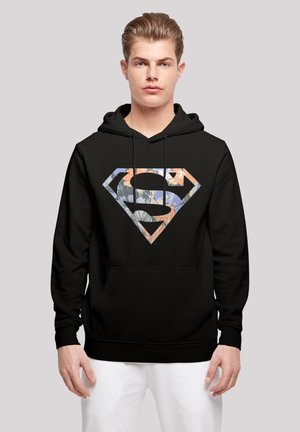 Svart hettegenser med et fargerikt diamantformet "S"-symbol med blomstermønstre. Designet står i kontrast til stoffets glatte tekstur.