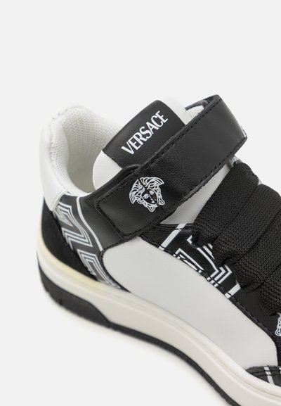 Svartvitt sneaker med läder- och textilmaterial, rund tå, vadderad krage, justerbar rem och Medusa-logotypdetalj.