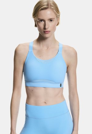 Woman wearing light blue sports bra and high-waisted leggings, standing against plain white background, facing forward with neutral expression.