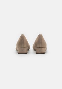 Zapatos de tacón bloque de ante beige con una textura suave, punta afilada y un mínimo detalle de costura en la parte trasera. Los tacones redondeados contrastan con el diseño elegante.