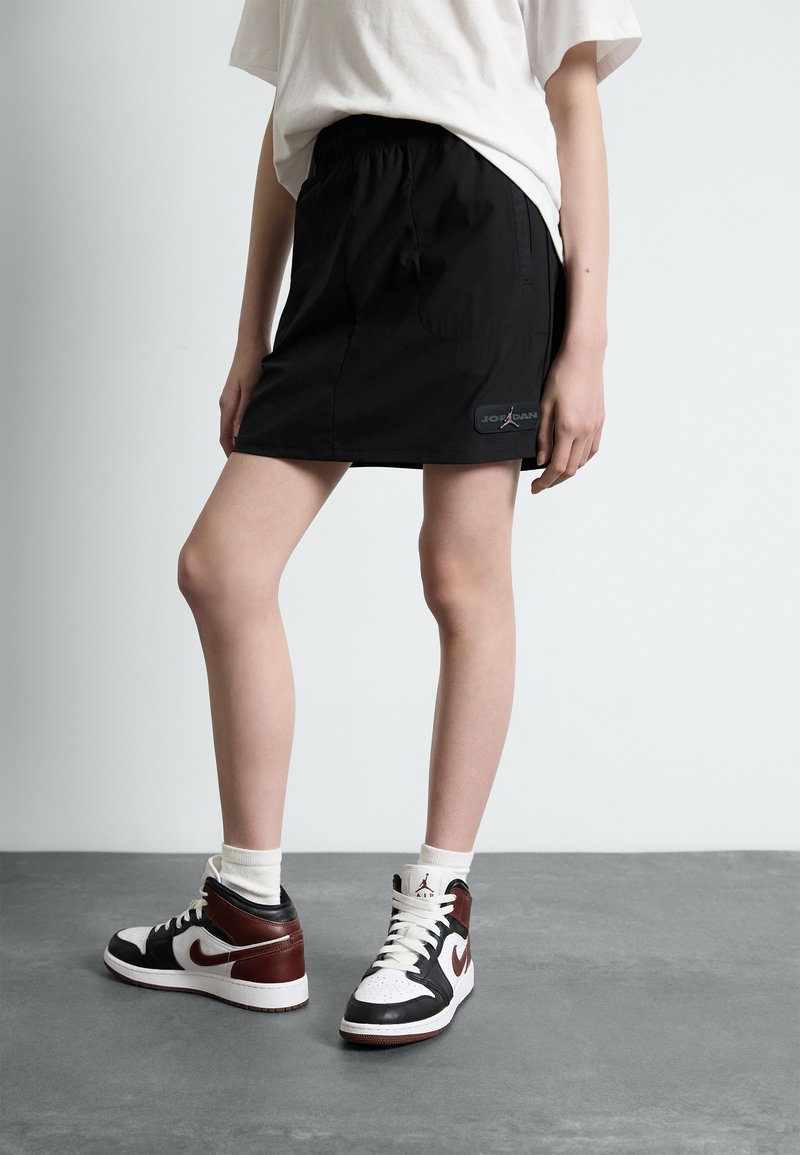Svart träningskjol med elastisk midjeband och sidofickor, tillsammans med svartvita hög-top sneakers med vinröda detaljer.