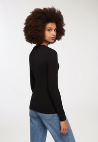 Czarny top z długim rękawem o dopasowanym kroju, gładkiej fakturze i okrągłym dekolcie, zestawiony z niebieskimi dżinsami w wysokim stanie.