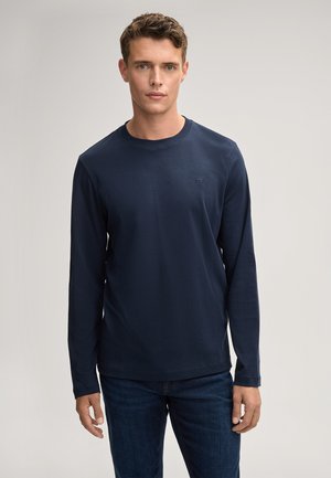 Marineblauwe longsleeve shirt van een gladde stof met een ronde hals en een klein geborduurd logo op de borst, gecombineerd met donkerdenim jeans.