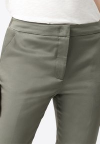 Pantaloni su misura verde oliva con una texture liscia, caratterizzati da una parte anteriore piatta, tasche laterali e un design della vita pulito.