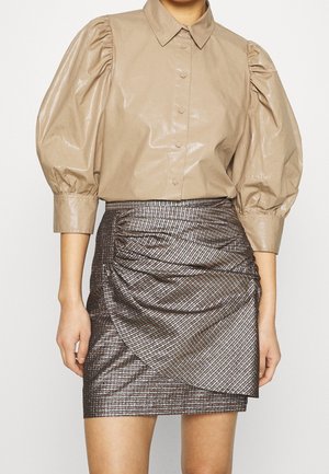 Beige overhemd met knopen en pofmouwen, gecombineerd met een hooggetailleerde metallic mini-rok met geplooide details en diagonale strepen.