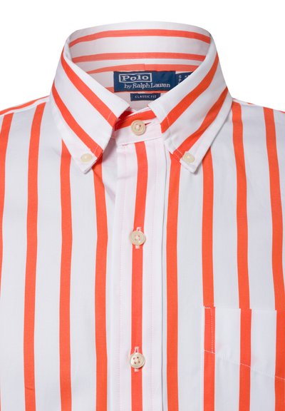 Witte blouse met oranje verticale strepen. Voorzien van een klassieke kraag, twee knopen en een borstzak. Zachte textuur.