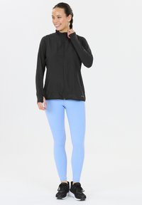 Svart zip-up jacka, långärmad, med en slät textur; tillsammans med ljusblå leggings med prickade linjer och svarta sportskor.