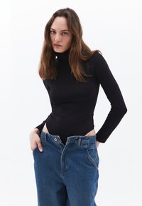 Schwarzer Langarm-Bodysuit mit hohem Kragen, kombiniert mit übergroßen blauen Jeans aus Denim mit Knopf- und Reißverschluss.