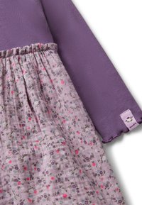 Maglione lungo a maniche ribattute di colore viola con una gonna a stampa floreale arricciata di un lilla chiaro, con accenti rosa e verdi, e un'etichetta cucita.