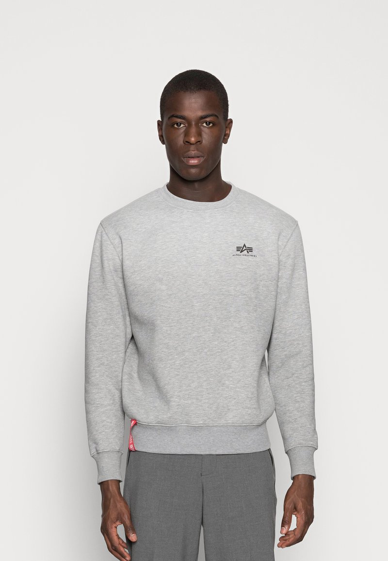 Grå sweatshirt lavet af blødt stof, med rund hals, ribbede manchetter og kant, med et lille sort logo på brystet og et rødt mærkat på siden.