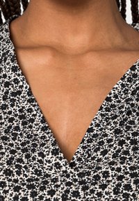 Tessuto a fantasia floreale con design a scollo a V in bianco e nero. Presenta una superficie morbida e strutturata. Visione ravvicinata di scollo e colletto.