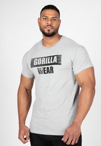 Grijze katoenen T-shirt met een opvallende zwarte "GORILLA WEAR" grafiek gecentreerd aan de voorkant. Korte mouwen en een ronde halsontwerp.