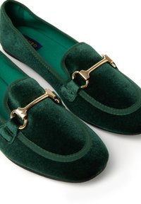 Zapatos de lona verde terciopelo con un acento de hardware dorado y punta redonda, con un acabado de textura suave y suelas planas.