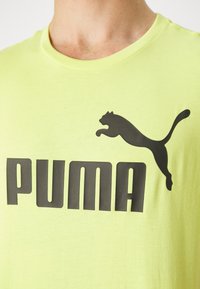 Nærbillede af en person iført en lysegrøn T-shirt med et stort sort Puma-logo og springende kat-emblem på brystet.