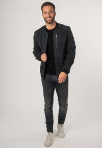 Navy suède bomberjack met ribgebreide manchetten en kraag, voorzien van ritszakken. Gecombineerd met donkere denim jeans en witte sneakers.