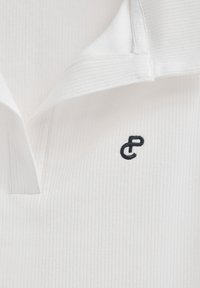 Camicia bianca con colletto e texture a coste; presenta un logo ricamato nero in contrasto sul petto. Design pulito e tessuto leggero.