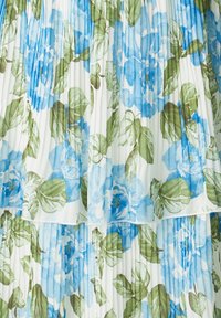 Robe florale présentant une base blanche avec des roses bleues et des feuilles vertes. Le tissu est plissé, mettant en valeur un design en couches.