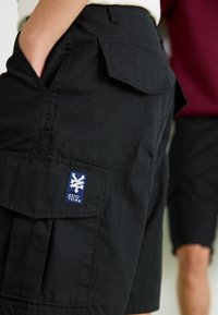 Sorte cargo shorts lavet af tekstureret stof, med sidelommer og et blåt logo-patch med teksten "Zoo York." Designet inkluderer sikret syning.