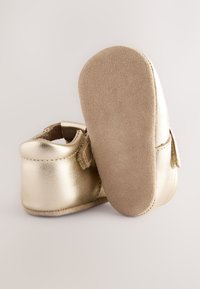 Chaussures bébé en cuir doré avec une finition lisse, semelles en daim, forme arrondie et une bride pour un ajustement sécurisé.