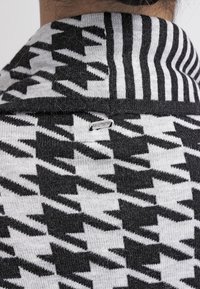 Pletený svetr s houndstooth vzorem v černobílé barvě, s žebrovaným límcem. Štítek viditelný u výstřihu. Měkká textura.