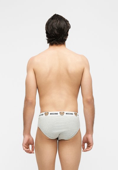 Άνδρας με σκούρα μαλλιά, που φαίνεται από πίσω, φορά γκρι εσώρουχα με λευκή μέση που φέρει πρόσωπα αρκουδάκια και κείμενο "MOSCHINO".
