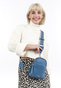 Blue textured crossbody bag with a silver zipper, adjustable strap, and compact design. Worn against a black floral-patterned skirt.