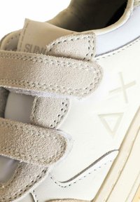 Sneaker bianco in materiale scamosciato e pelle, con cinturini in Velcro, accenti testurizzati e un design minimalista con motivi geometrici.