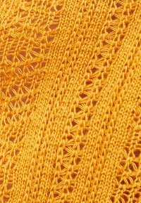 Stickad tyg i stark gul, med ett spetsmönster som har öppna stygn och strukturerade trådar, vilket ger ett lätt och luftigt utseende.