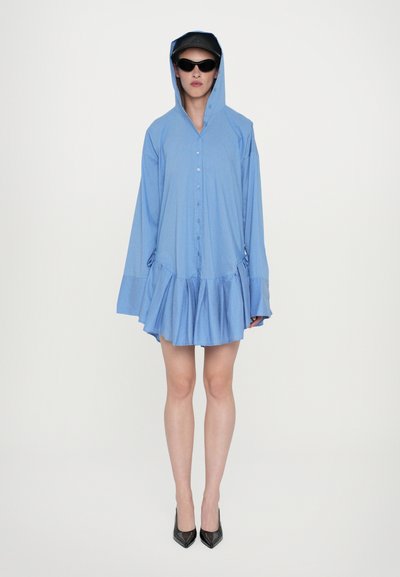 Abito button-up azzurro chiaro con cappuccio, orlo arricciato e maniche lunghe. Presenta un tessuto texturizzato ed è abbinato a tacchi alti neri.