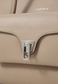 Sac à main en cuir beige avec finition texturée, dotée d'un fermoir en métal argenté et d'un branding subtil à l'avant.