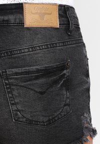 Black denim shorts featuring a frayed hem, back pocket with a curved seam, and a tan leather brand tag on the waistband.