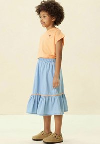 Haut orange à manches courtes avec un petit motif brodé, associé à une jupe tiered bleu clair avec un ourlet volanté et une taille élastique.
