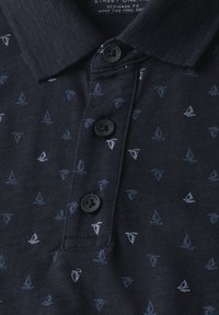 Námořnická modrá polo tričko z texturované tkaniny s vzorem malých grafických jachet v různých odstínech modré a bílé, s černými knoflíky.