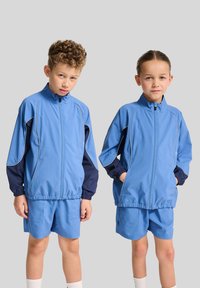 Ljusblåa träningsdräkter med mörkblå detaljer, bestående av en zip-up jacka och shorts, tillverkade av ett mjukt material och designade för komfort.